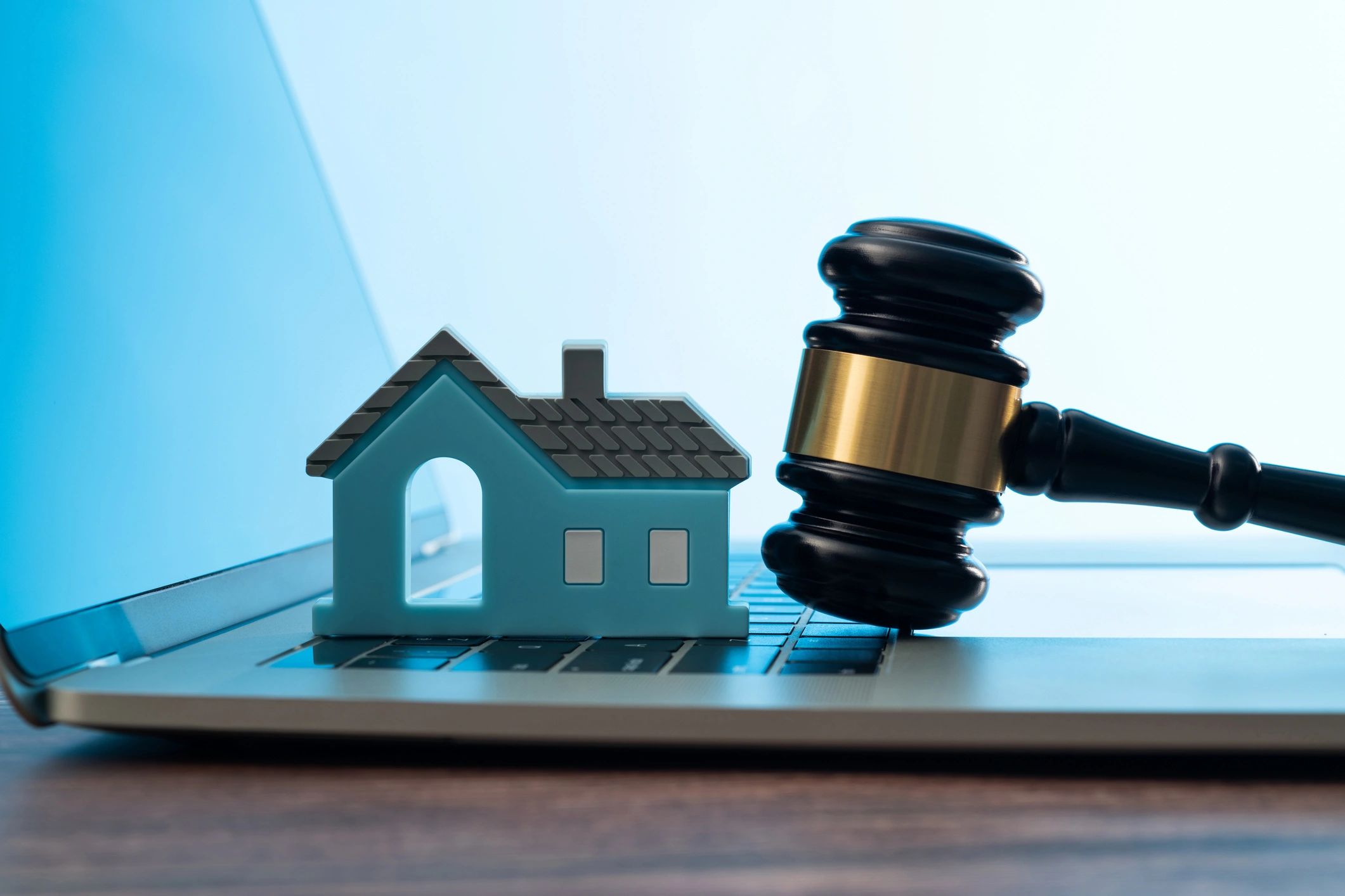 Gavel and model house on a laptop keyboard representing online auctions